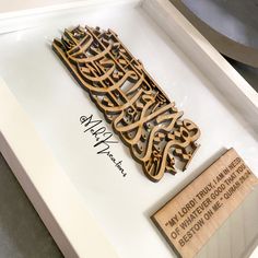 an arabic calligraphy on display in a white frame with a wooden sign that reads my lord trial