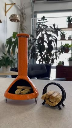 an orange fire pit next to a stack of logs on a table in front of a potted plant