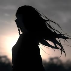 the silhouette of a woman with her hair blowing in the wind