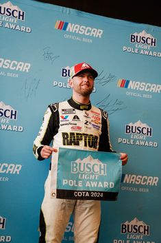 a man holding up a sign in front of a blue wall with the nascar pole award on it