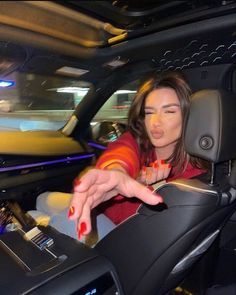 a woman sitting in the driver's seat of a car with her hand on the steering wheel