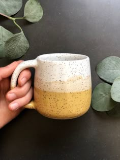 a hand is holding a coffee mug on a table next to some leaves and plants