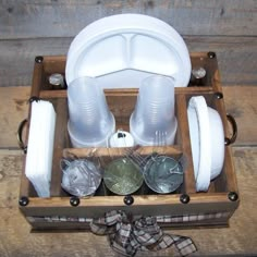 a wooden box filled with white dishes and cups on top of a table next to a bow tie