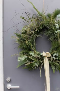 a wreath is hanging on the front door with a ribbon tied around it and surrounded by greenery