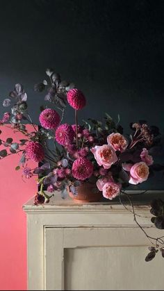 a vase filled with pink flowers sitting on top of a white dresser next to a pink wall