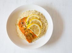 a white plate topped with fish and lemons on top of couscouse