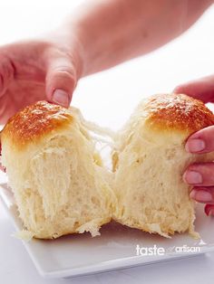 two hands are grabbing the top half of a piece of bread on a white plate