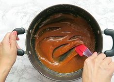 two hands are stirring chocolate into a saucepan with a red spatula in it