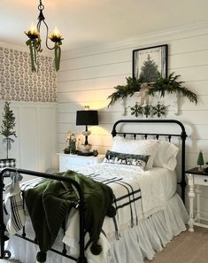 a bedroom with white walls and black iron bedspread, green throw pillows on the bed