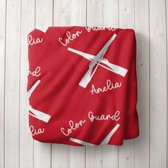 a red blanket with white writing on it sitting on top of a wooden floor next to a pair of scissors