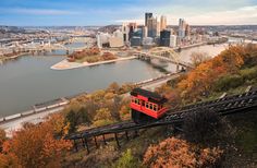 a red train is going down the tracks in front of a large city and river