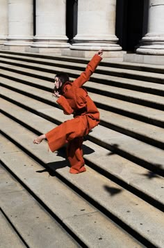 a woman in an orange outfit is dancing on some steps with her hand up to the side