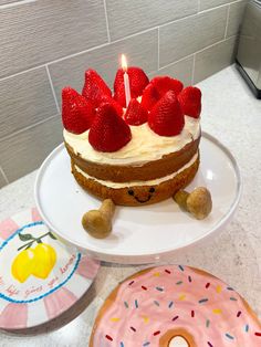 a birthday cake with strawberries on top sits next to a doughnut and candle