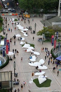 an aerial view of people walking down the street with giant white objects on display in front of them