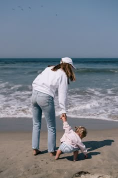 a woman holding the hand of a small child on top of a sandy beach next to the ocean