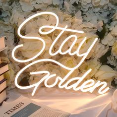 a sign that says stay golden on top of a table with books and flowers in the background