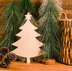 three wooden christmas trees sitting on top of a table next to baskets and pine cones