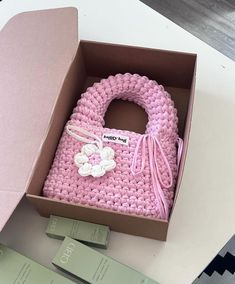 a pink crocheted purse in a box with tags on the front and side