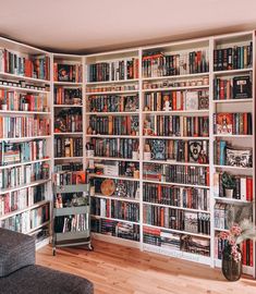 a room filled with lots of books on top of white shelves next to a gray couch