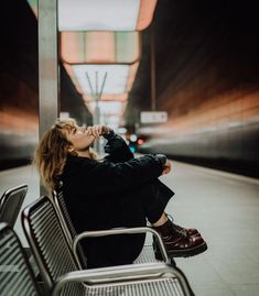 a woman sitting on top of a metal bench next to a train station platform with her eyes closed