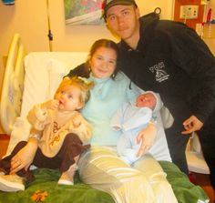 a man standing next to two girls and a baby in a hospital bed with an infant on her lap