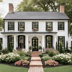 a white house with black shutters and lots of flowers in the front yard,