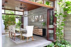 a dining room table with white chairs next to an open patio door and plants on either side