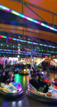 two people riding bumper cars in an indoor area with colorful lights on the ceiling behind them