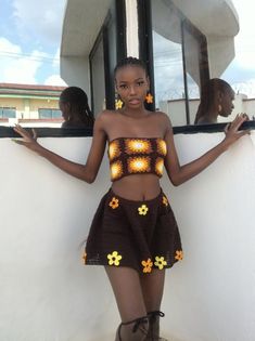 a woman standing in front of a window with her hands on her hips, wearing a brown and yellow crop top