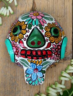 a colorfully painted skull sitting on top of a wooden table next to white flowers