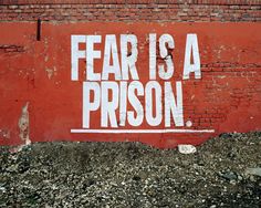 a red brick wall with the words fear is a prison painted on it's side