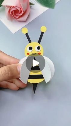 a person holding a paper cut out of a bee with a flower in the background