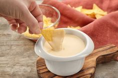 a person dipping some food into a small white bowl on top of a wooden tray