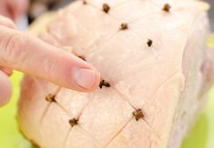 a person pointing at some tiny black bugs on a piece of meat