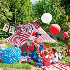 children sitting on the ground in front of a circus tent with balloons and streamers