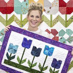 a woman holding up a quilt with flowers on it