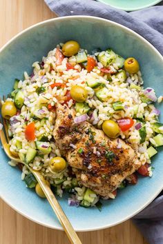 a blue bowl filled with rice, meat and olives next to a fork on top of it