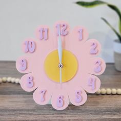 a pink clock with numbers on it sitting on a table next to a potted plant