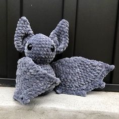 a crocheted gray stuffed animal sitting on the ground next to a black door