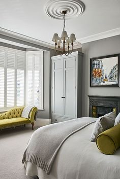 a bedroom with gray walls and white shutters, a yellow couch, and a fireplace