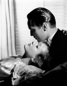 a man and woman laying on top of each other in front of a window with curtains