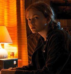 a woman sitting at a table with a lamp in front of her and an electronic device to the side