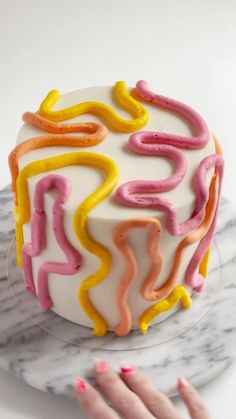 a white cake with pink, yellow and orange icing on it's side