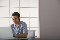 a man sitting at a table with a laptop in front of his face and smiling