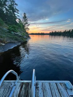 a dock on the edge of a body of water with trees in the background at sunset