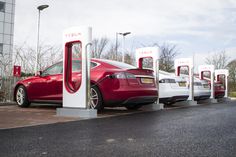 four tesla electric cars are charging at a gas station