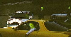 two men in green masks are behind the wheel of a yellow car