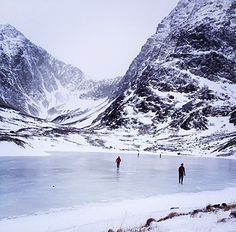 two people skating on an icy lake with mountains in the background and snow covered ground