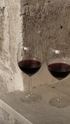 two glasses of red wine sit on a ledge