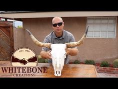 a man sitting on top of a wooden table next to a bull skull